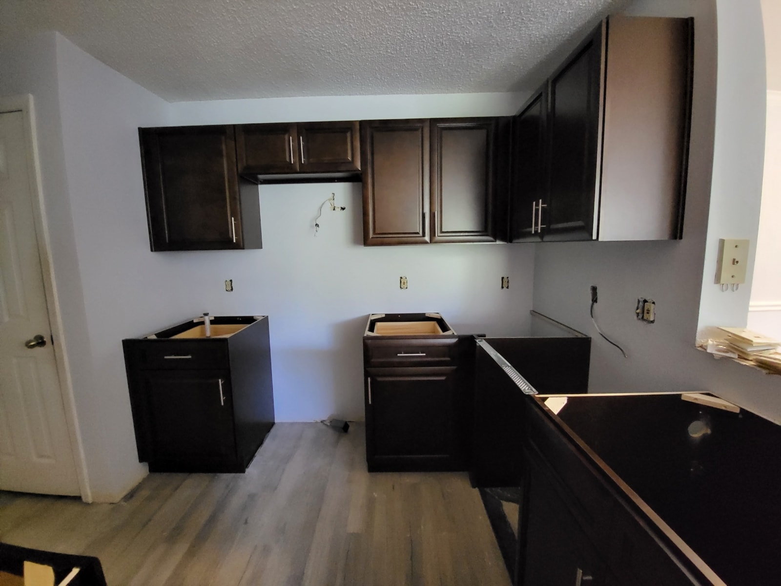 Dark espresso raised panel kitchen under construction with upper and lower cabinets on light wood floors by 1 Stop Cabinets
