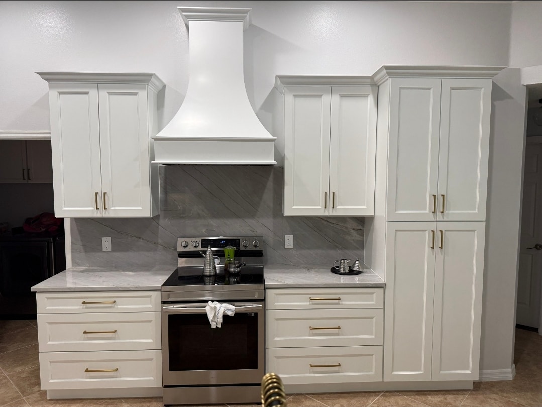 White raised panel kitchen with custom range hood marble slab backsplash stainless range tall pantry and gold hardware by 1 Stop Cabinets