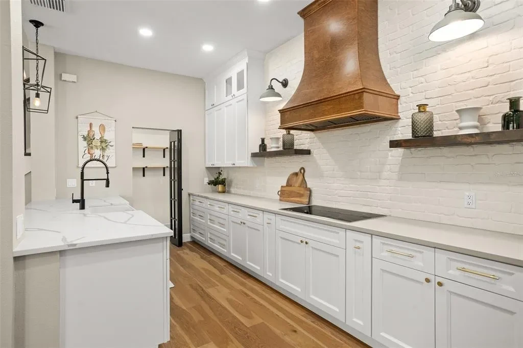 White shaker kitchen with wood range hood and white brick backsplash by 1 Stop Cabinets
