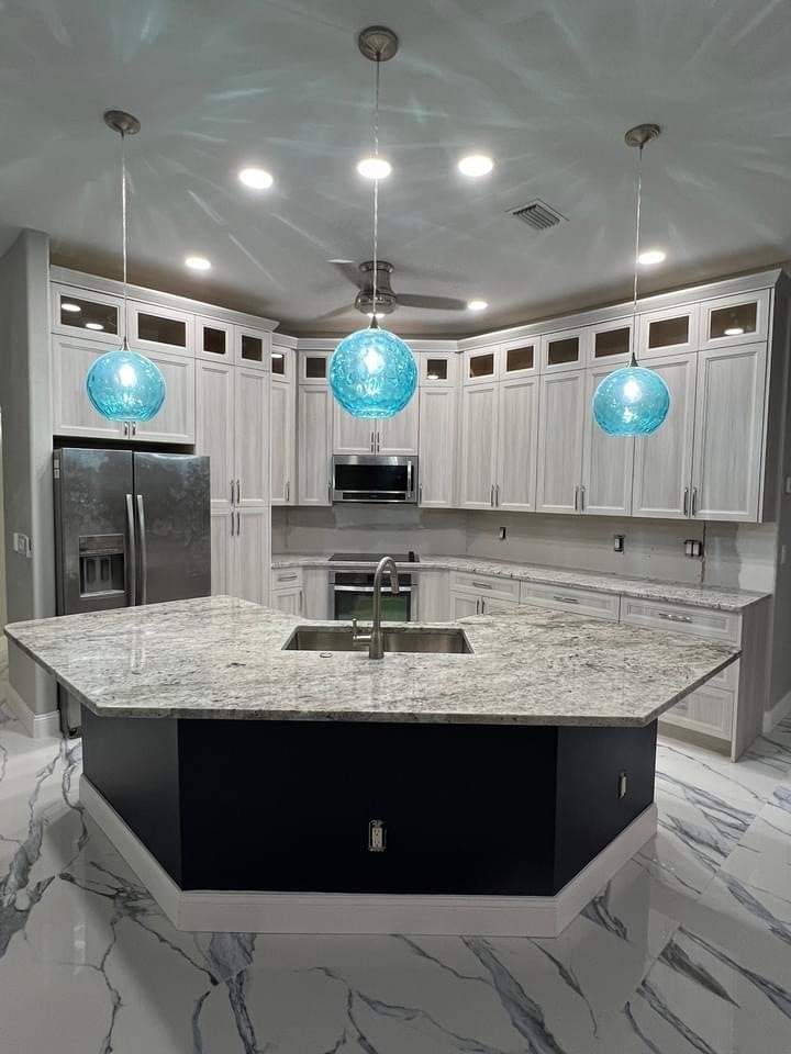 White raised panel kitchen with turquoise pendant lights and granite island by 1 Stop Cabinets