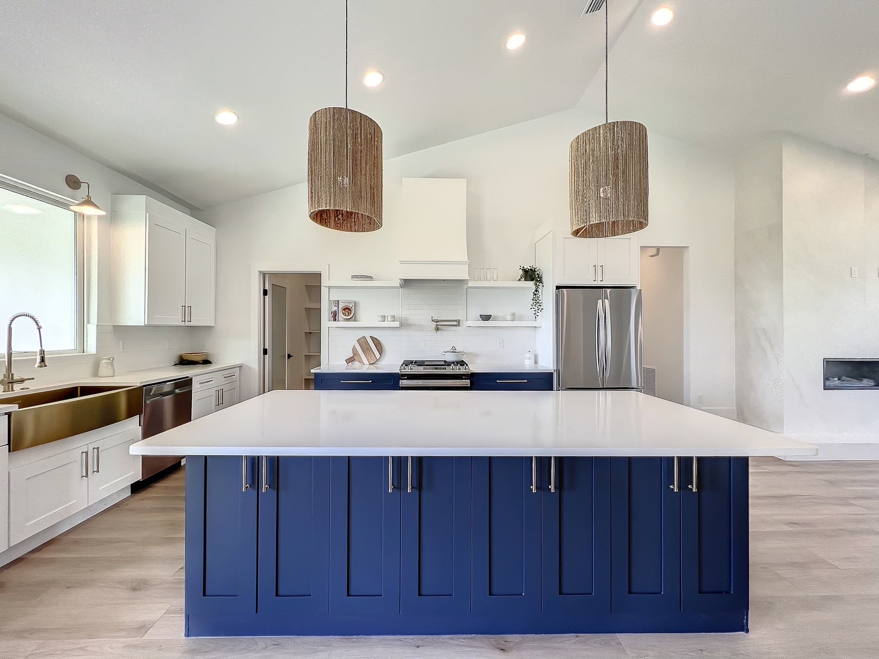 White and navy blue two-tone kitchen with large quartz island rattan pendants and brass farmhouse sink by 1 Stop Cabinets